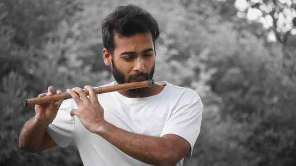Bansuri player playing music in sunshine at Park - Indian Flute Player