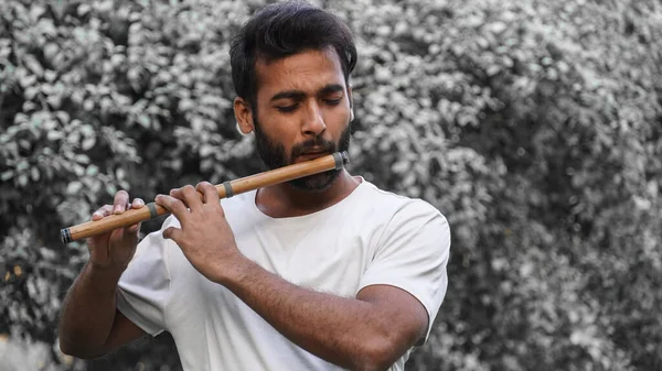 Bansuri player playing music in sunshine at Park - Indian Flute Player