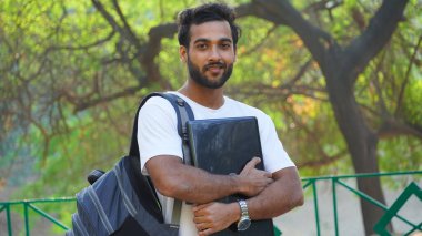 Kampüste dizüstü bilgisayarı ve çantası olan genç bir adam.