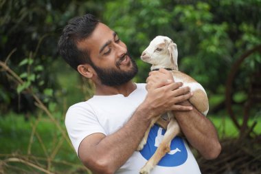 Bir adam elinde bir keçi tutuyor.