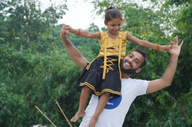 Bir oğlan omzuna küçük şirin bir kız yerleştirmiş ve ikisi de gülümsüyor.