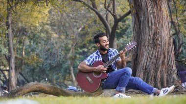 Gitarlı ve parkta gitar çalan genç bir çocuk.