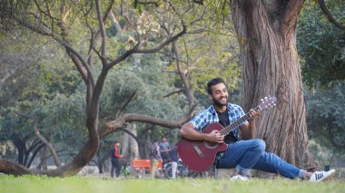 Gitarlı ve parkta gitar çalan genç bir çocuk.