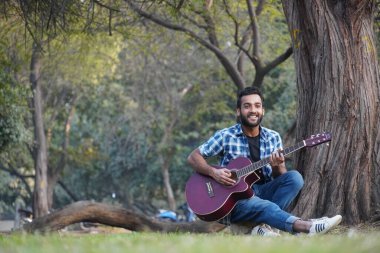 Gitarlı ve parkta gitar çalan genç bir çocuk.