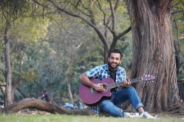 Gitarlı ve parkta gitar çalan genç bir çocuk.