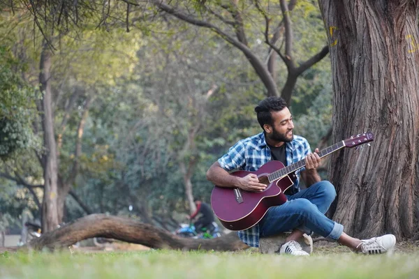 Gitarlı ve parkta gitar çalan genç bir çocuk.