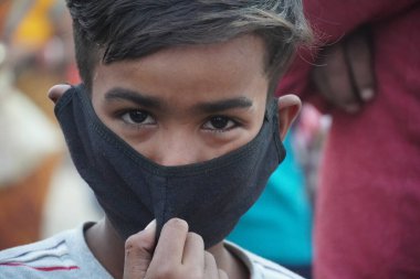 Bir çocuk maske takıyor ve kamera izliyor.