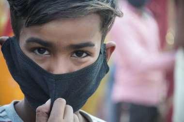 Bir çocuk maske takıyor ve kamera izliyor.