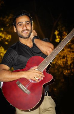 Gitarı olan bir adam kamerayı izliyor.