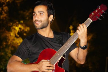 Gitarı olan bir adam kamerayı izliyor.