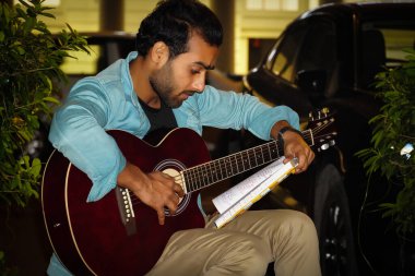 Gitar çalan ve notlarını okuyan bir gitarist.