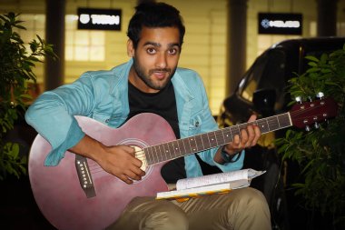 Kırmızı gitarlı bir çocuk kameraya bakıyor ve gergin.