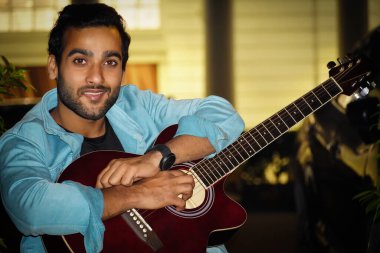 Kırmızı gitarlı bir adam kameraya bakıyor ve gülümsüyor.