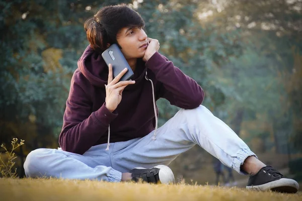 都市公園の芝生の上に座って電話で話している男子生徒 — ストック写真