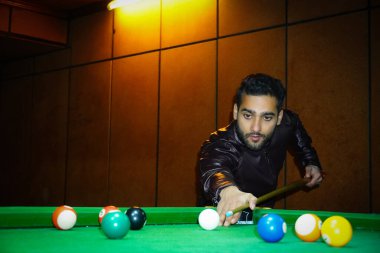 Kulüp binasında elinde sopa ve topla bilardo masası olan bir adam.