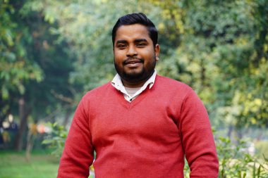 Genç adam sabah iş yerinde parkta durup gülümsüyor.