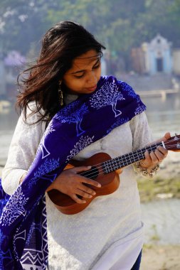 Bahçede gitar çalan bir kadın. Bulanık bahçe / park geçmişi olan ukulele oynayan kadınlar.