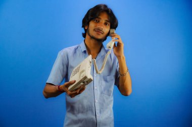 Yakışıklı genç adam mavi arka planda telefonla konuşuyor.