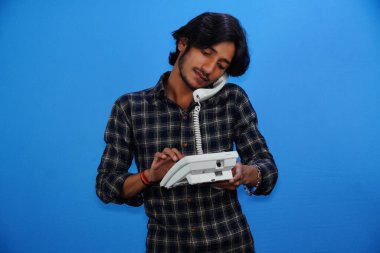 Yakışıklı genç adam mavi arka planda telefonla konuşuyor.