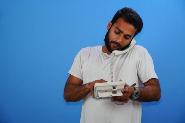 Yakışıklı genç adam mavi arka planda telefonla konuşuyor.