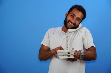 Yakışıklı genç adam mavi arka planda telefonla konuşuyor.