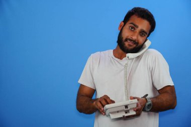 Yakışıklı genç adam mavi arka planda telefonla konuşuyor.