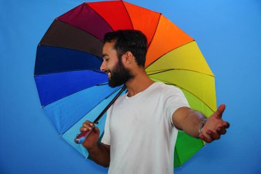 Genç yakışıklı adam renkli bir şemsiye tutuyor ve hayret verici bir ifade veriyor, korku ve heyecan dolu bir yüz..