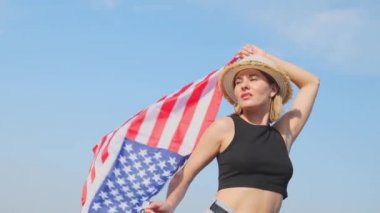 Bottom view of a young woman holding a USA flag against a blue sky. Slow motion portrait. Holiday in America. Independence Day
