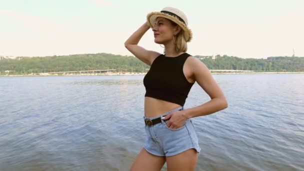 Young Woman Short Shorts Black Shirt Hat Stands Beach River — Vídeo de Stock