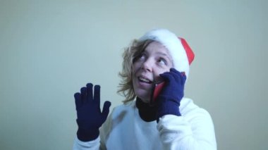 Kırk yaşında beyaz kazaklı ve kırmızı yeni yıl şapkalı bir kadının portresi. Ağır çekim portresi. Yeni yıl tatili. Mutlu Noeller.