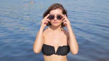 Portrait of a young woman in sunglasses and a black bathing suit on a background of water with waves. slow motion. Swimming at sea