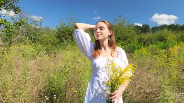一位身穿白衣的年轻女子走进植物园 一个带着一束花的快乐女人的画像 — 图库视频影像