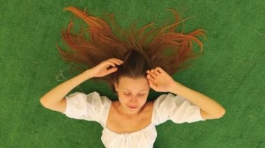 Yeşil arka planda beyaz elbiseli neşeli bir kadının portresinin üst görüntüsü. Kadın dinleniyor.