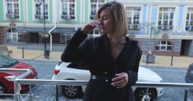 Siyah elbiseli genç bir kadın şehrin güzel binalarının yanında duruyor. Başkentte dolaşın.