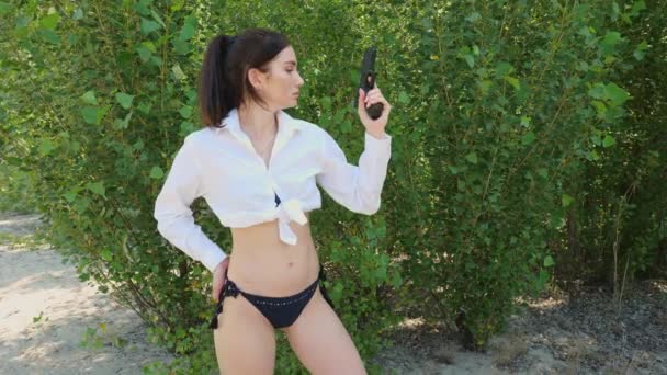 穿着白衬衫和黑色内裤拿着枪的年轻女人 布鲁内特女人享受大自然的乐趣 — 图库视频影像