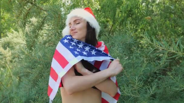 アメリカの国旗のついた赤い新年の帽子の若いブルネットの女性の肖像画 黒水着姿の女が休んでいる — ストック動画