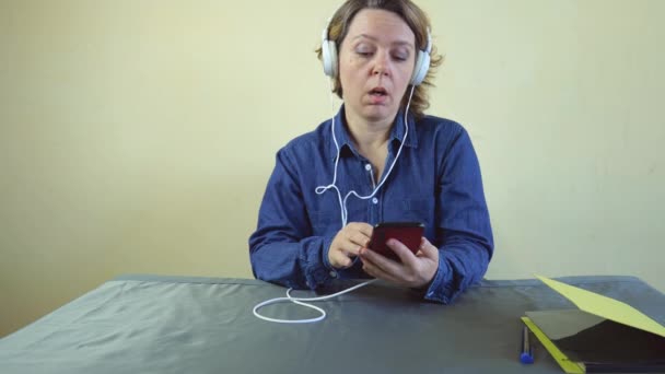 Μια Σαραντάχρονη Γυναίκα Τζιν Πουκάμισο Λευκά Μεγάλα Ακουστικά Κοιτάζει Ένα — Αρχείο Βίντεο