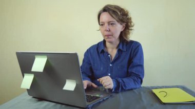 Mavi tişörtlü yetişkin bir kadın dizüstü bilgisayarda çalışıyor. Serbest çalışan kadın portresi