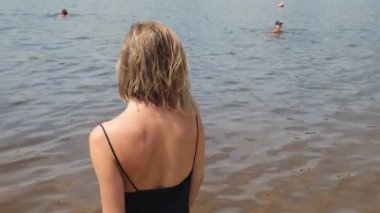 Siyah ıslak elbiseli bir kadının güzel omuzlarının dikiz manzarası. Suyun kenarında bir kadının portresi. yavaş çekim