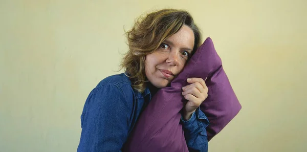 An adult forty-year-old woman hugs a purple pillow. Portrait of a woman with big eyes