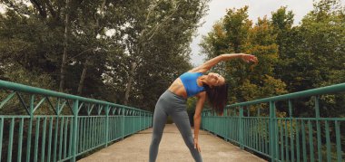 Genç atletik Asyalı kadın doğa arasında bir köprüde geriniyor. Bir spor kadının portresi. Doğada kadın eğitimi