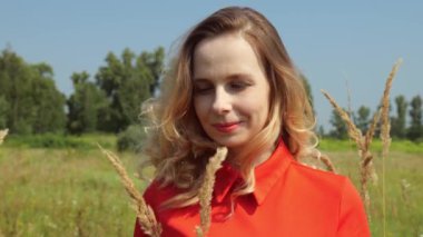 Kuru bitkilerin arasından tarlada kırmızı elbiseli sarışın bir kadının portresine bakın. Bir kadının yavaş hareket eden portresi. Sahada yürüyen bir kadın