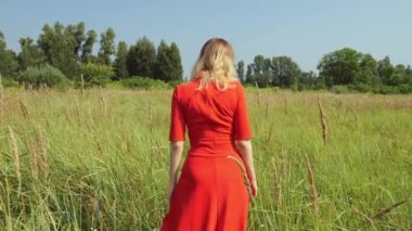 Kırk yaşında, kırmızı elbiseli bir kadın tarlada yürüyor. Ağır çekim. Doğada dinlenen kadın