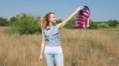 Kırk yaşında kot elbiseli bir kadın doğada dururken ABD bayrağını sallıyor. Bağımsızlık Günü 4 Temmuz.