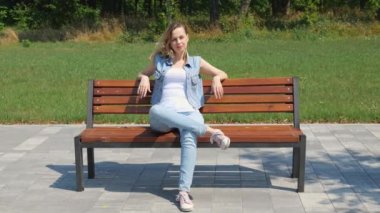 Kırk yaşında kot giyen bir kadın parkta bir bankta oturuyor. Kadın bir yetişkin. yavaş çekim