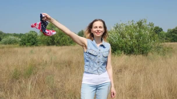 デニムの服を着た若い女性が自然に立っている 大人の女性は手にアメリカ国旗を持っている スローモーションポートレート — ストック動画