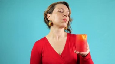 A portrait of a forty-year-old woman in a red sweater holds a red candle on a blue background. female magic. slow motion