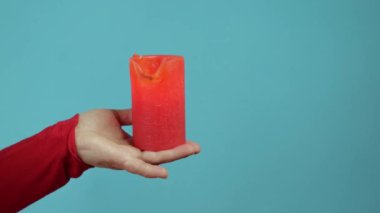 View of a woman's hand and a red candle on a blue background. slow motion