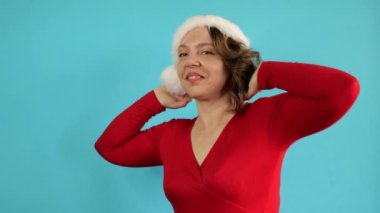 Portrait of a cheerful forty-year-old woman in a red jacket and a New Year's hat on a blue background. Slow motion portrait. New Year holiday