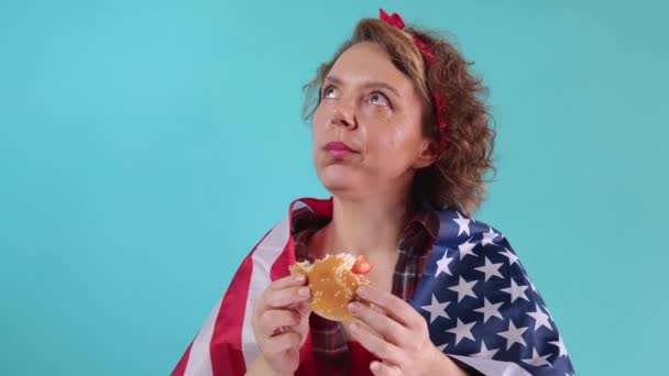 Forty Year Old Woman Flag Eats Burger Blue Background Slow — Stockvideo